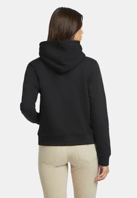 Sudadera negra con capucha de textura suave y puños acanalados. Presenta un corte clásico y un bolsillo canguro. Detalle de costura visible.
