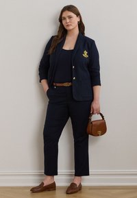 Marineblå dress med en figursydd blazer, gullknapper og emblem. Matchende bukser, brunt belte, brun håndveske og loafers fullfører antrekket.