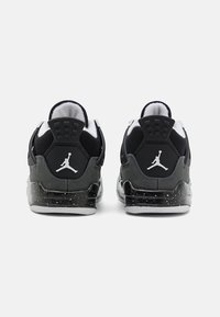 Scarpe sportive nere e grigie con upper testurizzato, colletto imbottito e dettagli bianchi. Presenta un logo visibile e una suola maculata.