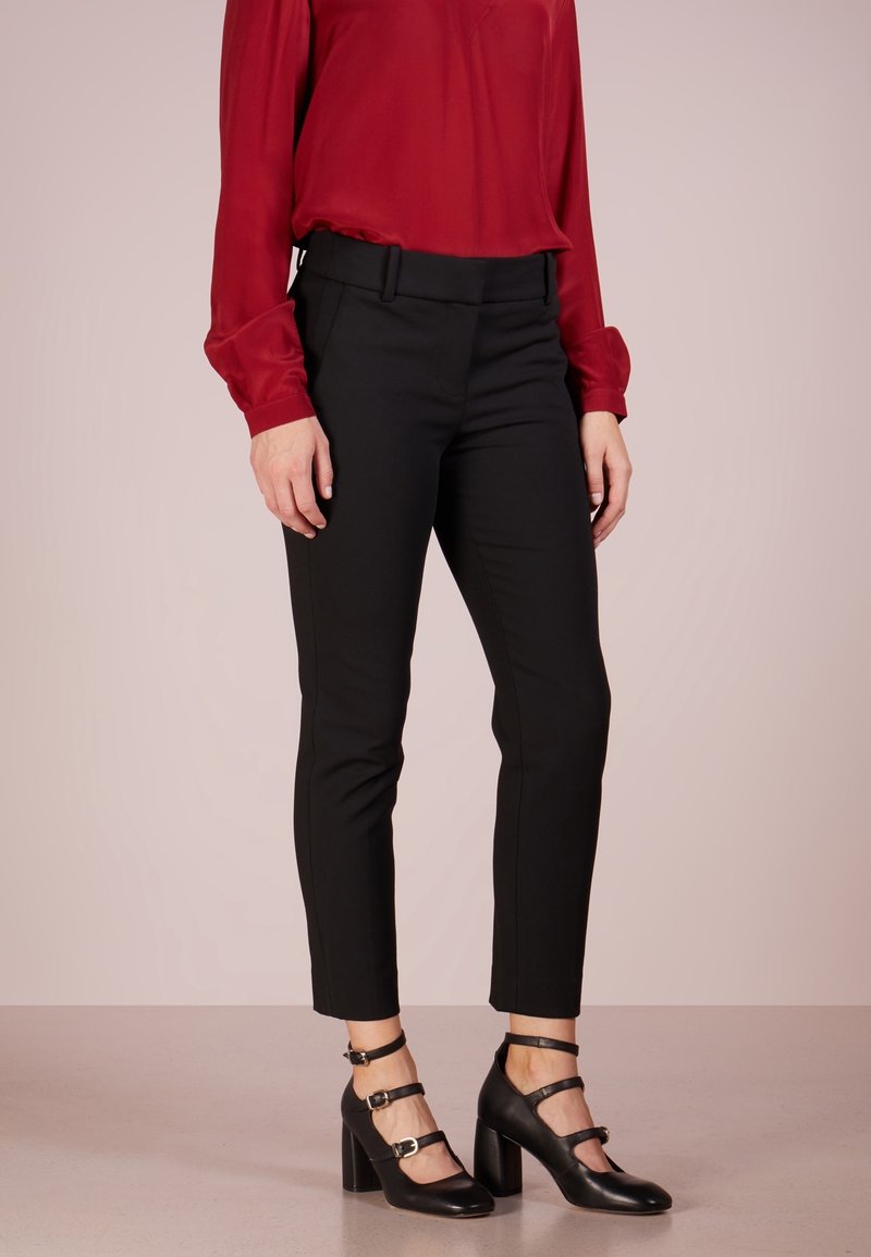 Pantalons taillés noirs à coupe slim, avec une texture lisse et une taille haute. Associés à un chemisier léger rouge vif et des chaussures à talons noires.