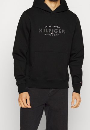 Hoodie noir en mélange de coton, avec une poche kangourou, des poignets côtelés et un logo graphique blanc et rouge sur la poitrine.