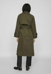 Oliwkowy trencz z paskiem w talii, podwójnym tyłem i mankietami, wykonany z gładkiego, trwałego materiału. Dopasowany fason.