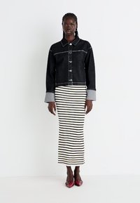 Black denim jacket with gray accents and buttons, paired with a striped black and white midi skirt, and red pointed-toe shoes.