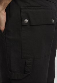 Fekete cargo sort, textúrált anyagból, két oldalsó zsebbel és egy snap gombbal záródó fedeles zsebbel a jobb combon.