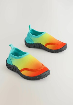 Des chaussures à enfiler de couleur vive présentent un dégradé allant du turquoise à l'orange, fabriquées en matériau flexible avec une semelle en caoutchouc noir texturé.