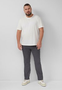 Weißes Baumwoll-T-Shirt, graue Baumwollhose, beiges Sneaker, steht vor einem einfarbigen Hintergrund. Einfaches Design, keine sichtbaren Muster oder Akzente.