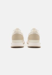 Zapatillas deportivas beige y blancas con acentos de cuero texturizado, diseño minimalista y detalles de tela en la lengüeta y la pestaña del talón.