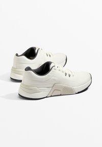 Białe buty sportowe z teksturowaną tkaniną, czarnymi akcentami i solidną gumową podeszwą. Charakteryzują się niskim profilem i sznurowanym wzorem.