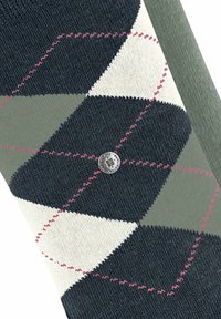 Skarpety o fakturowanym wzorze geometrycznym w odcieniach granatu, kremu i zieleni, z różowym przeszyciem i okrągłym metalowym logo na środku.