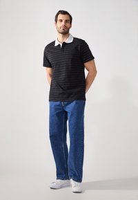 Svartstripete polo skjorte med hvit krage, kombinert med blå rette jeans og hvite joggesko. Enkelt, uformelt design.