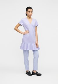 Φόρεμα λεβάντας με V-λαιμόκοψη και κοντά μανίκια, με φουσκωτή ραφή στο κάτω μέρος. Συνδυασμένο με ανοιχτό μπλε παντελόνια και μαύρα παπούτσια. Λεία υφή.