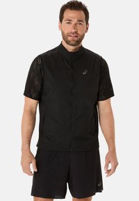 Sort atletisk vest med høj krave, let materiale og netdetaljer på de korte ærmer, parret med sorte shorts med teksturdetaljer.