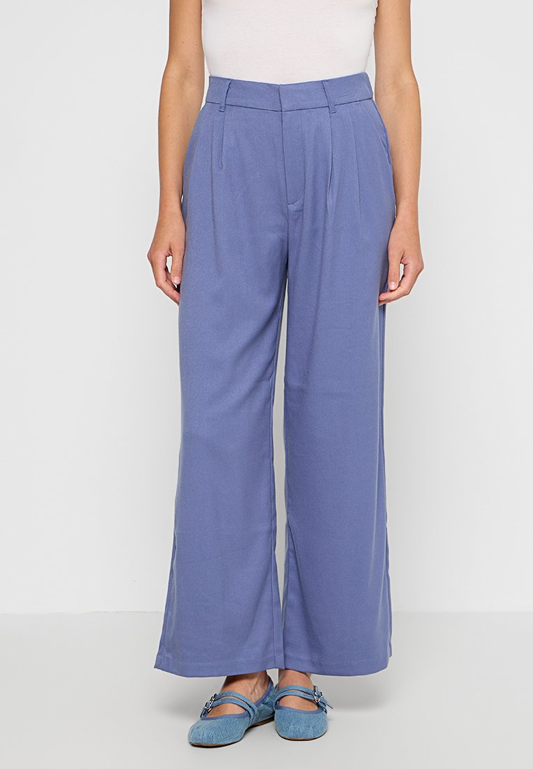 Spodnie z wysokim stanem i szerokimi nogawkami z jasnoniebieskiego materiału. Posiadają fałdy z przodu, bezszwowe kieszenie i gładką teksturę. Idealne do codziennych stylizacji.