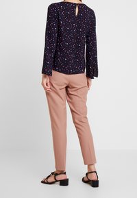 Blusa blu navy con una piccola stampa di cuori multicolori, maniche lunghe e dettaglio cut-out sul retro. Abbinata a pantaloni rosa chiaro su misura e sandali neri.