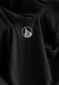 Giacca in pile nera con tessitura liscia, design arrotondato e tasca laterale con logo circolare bianco con la scritta "JOTT".