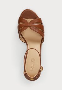 Rudi odiniai šlepetės su kryžminėmis dirželiais, atviru pirštu, kulkšnies dirželiu ir lygiu vidumi. Prekės ženklas matomas ant pado.