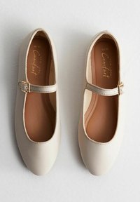 Zapatos Mary Jane de color beige claro en material sintético suave, con puntera redonda, correa al tobillo con un hebilla metálica y un diseño sencillo.