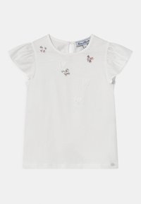 Valkoinen lyhythihainen toppi, jossa on röyhelöhihat. Edessä on värikkäitä brodeerattuja perhosia. Puuvillamateriaali, jossa on pyöreä pääntie.