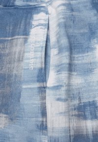 Tecido abstrato azul com padrão, de textura suave, apresentando um detalhe de logótipo visível em branco. O design inclui tons variados de azul e branco.