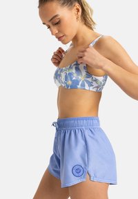 Blauer Blumen-Bikini-Top mit schmalen Trägern, kombiniert mit hellblauen Badehorts, die einen elastischen Bund und seitliche Schlitze für mehr Bewegungsfreiheit haben.