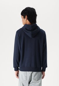 Marineblauwe hoodie met een trekkoordkap, zachte structuur, ribbelmanchetten en -zoom. Heeft een relaxte pasvorm, zichtbare stiksels op de naden en geen patronen.