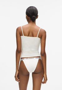 Camisole ajustée couleur crème avec fines bretelles, associée à un string assorti avec une ceinture noire « KARL LAGERFELD ». Texture lisse.
