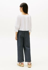 Blusa bianca corta con dettagli plissettati, abbinata a pantaloni a gamba larga a righe blu scuro. La calzatura presenta suole platform beige e cinturini alla caviglia.