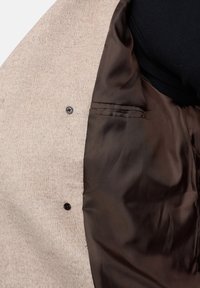 Beżowy płaszcz z wełnianej mieszanki z gładką brązową satynową podszewką, z czarnym guzikiem i eleganckim detalem kieszeni wewnętrznej.