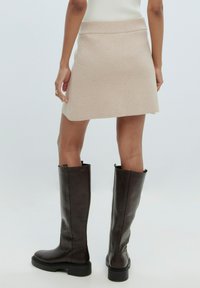 Jupe mini en maille beige avec une taille cintrée, associée à des bottes en cuir marron brillantes et hautes avec une semelle épaisse.