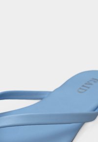 Ανοιχτό μπλε σανδάλι με δύο λεπτές λωρίδες και τυπωμένο το "PRADA" στη σόλα, εμφανιζόμενο από κοντινή πλευρική γωνία.