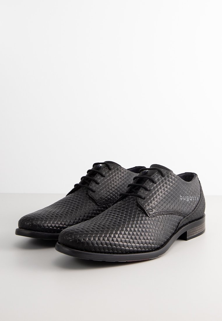 Zapatos de vestir negros con una parte superior de piel texturizada con un patrón de diamante, punta redonda y suela plana negra. Presenta un sutil logotipo en el lateral.