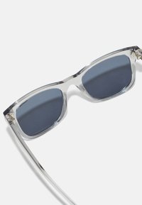 Ochelari de soare din acetat transparent cu lentile de culoare albastru închis, formă rectangulară, brațe subțiri transparente și detalii hardware de ton argintiu.