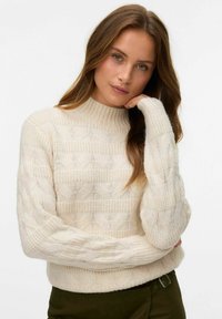 Sweter dzianinowy w kremowym kolorze z wysokim kołnierzem i teksturowanym wzorem w warkocze. Posiada prążkowane mankiety i dół, wykonany z miękkiego materiału z otwartymi splotami.