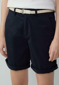 Shorts en coton bleu marine avec des revers roulés, dotés d'une ceinture en crème tressée avec une boucle en métal et de poches avant. Design classique décontracté.