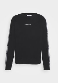 Felpa nera con polsini e orlo a coste. Presenta il logo "Calvin Klein" in bianco sul petto e strisce laterali a contrasto con branding ripetuto.