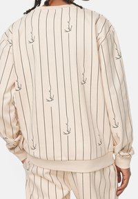 Felpa color crema con strisce verticali nere e motivi astratti. Presenta polsini e orlo a coste, con una trama di tessuto morbido.