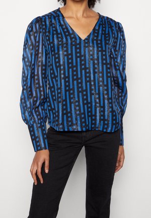 Blusa a fantasia blu con scollo a V, caratterizzata da strisce orizzontali e verticali in diverse tonalità di blu e dettagli metallici. Maniche lunghe e strutturate.