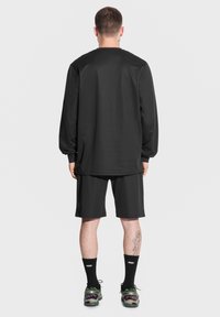 Czarna koszula z długim rękawem i szorty, obie z gładkiego materiału. Noszone z czarnymi skarpetkami i wielokolorowymi butami sportowymi.