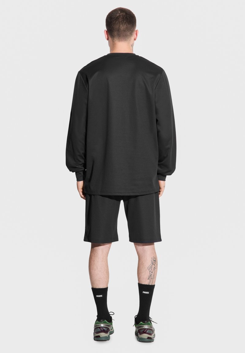 Czarna koszula z długim rękawem i szorty, obie z gładkiego materiału. Noszone z czarnymi skarpetkami i wielokolorowymi butami sportowymi.