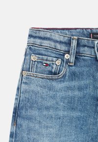 Jeans in denim azzurro chiaro con design classico a cinque tasche, ferramenta argentata e una toppa con marchio caratterizzata da accenti rossi, bianchi e blu.