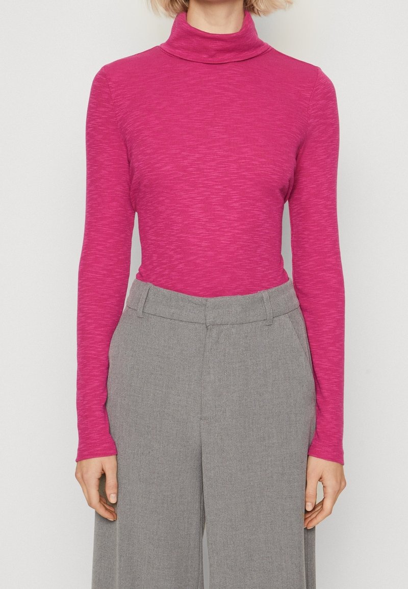 Tight turtleneck-top i livlig magenta med ett texturerat mönster, kombinerat med hög midja grå byxor i slätt tyg med veck.