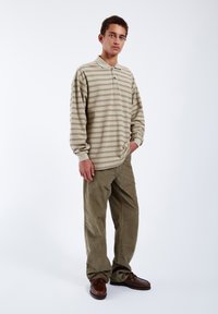 Beige polo s dlouhým rukávem s horizontálními hnědými pruhy, doplněný olivovými manšestrovými kalhotami a hnědými šněrovacími botami.