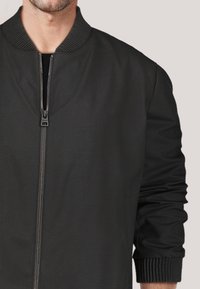 Schwarze Bomberjacke mit Reißverschluss vorne, geripptem Kragen und Bündchen, aus einem glatten Material mit minimalen Verzierungen.
