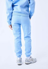 Pantalones de chándal azul claro con puños y cintura acanalados, combinados con zapatillas deportivas plateadas. El tejido parece suave y liso.