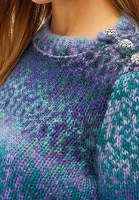 Strickpullover in Lila- und Türkistönen, mit rundem Ausschnitt und drei dekorativen Edelsteinen an der Schulter.