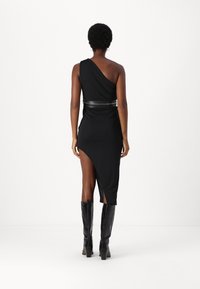 Abito nero a spalla unica con design drappeggiato, orlo asimmetrico, accentuato da una cintura nera e abbinato a stivali neri lucidi fino al ginocchio.