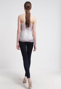 Biała półprzezroczysta koszulka na cienkich ramiączkach z kwiatowym wzorem, zestawiona z ciemnymi obcisłymi dżinsami i jasnobeżowymi szpilkami.