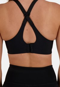 Svart sport-bh med perforerat mönster, justerbara korsryggsremmar och en krokstängning på baksidan. Slät, elastisktygtextur.