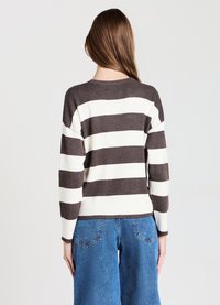 Brown and white striped sweater with ribbed texture, round neckline, and long sleeves. Paired with high-waisted blue denim pants.