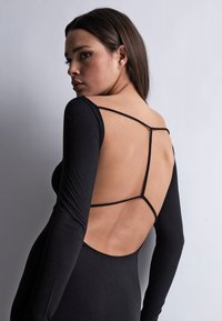 Body noir à manches longues avec un dos ouvert et des fines bretelles, présentant une coupe ajustée et une texture lisse.